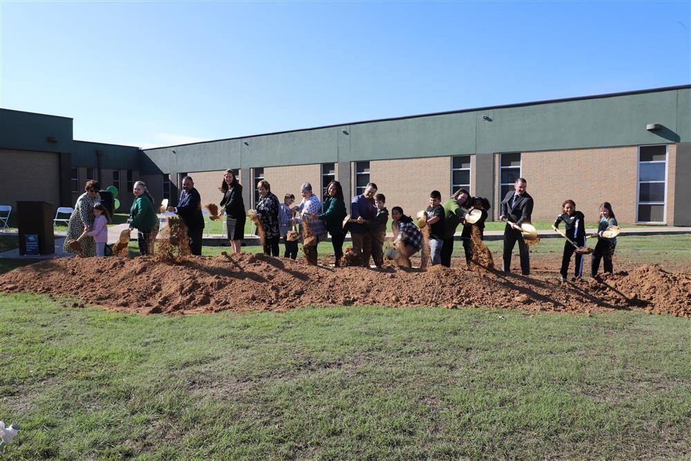  Students and adults with shovels turning dirt. 